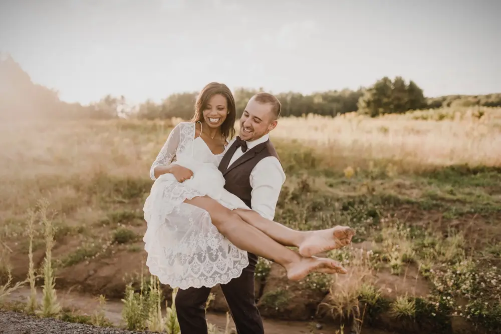 Groom carrying his bride through a summer field